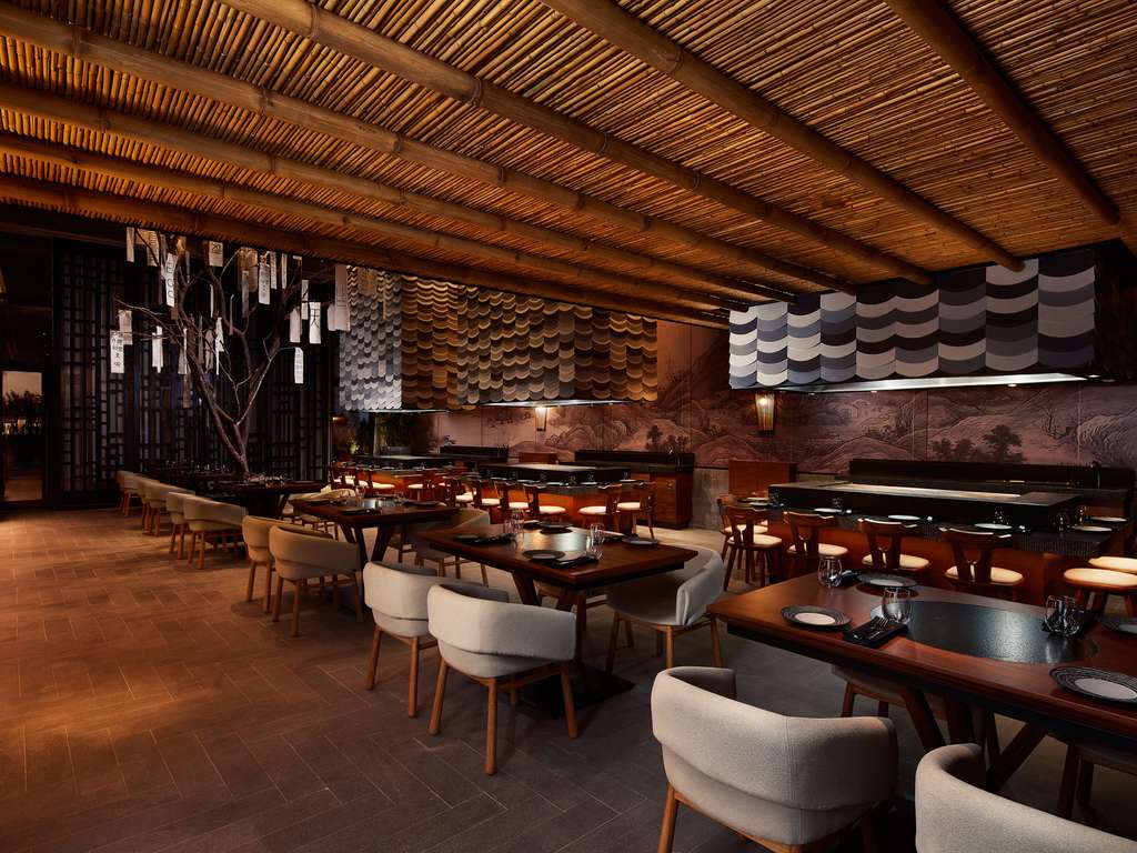 Modern restaurant interior at SLS Playa Mujeres with wooden slatted ceiling, cream chairs, dark wood tables, and textured wall panels.