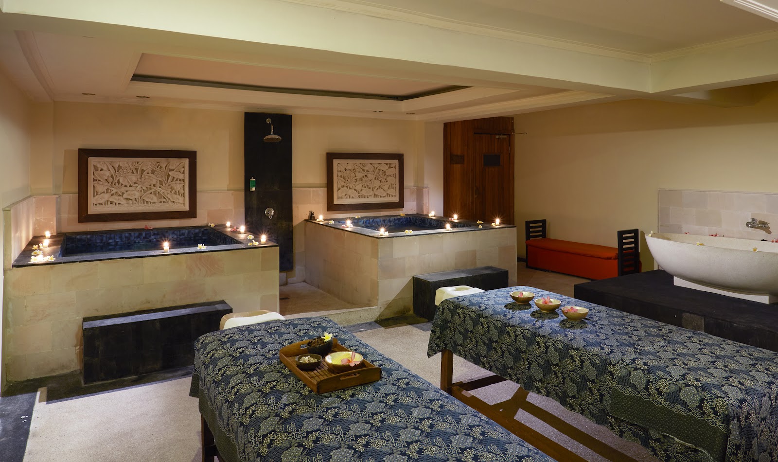 Spa treatment room with two massage beds, soaking tubs with candles, and framed botanical artwork on cream walls.