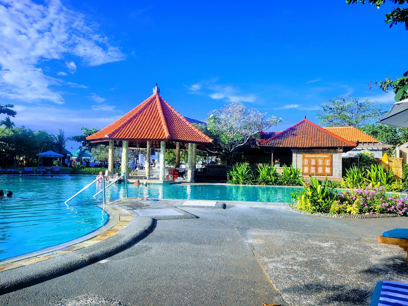 Turquoise pool with thatched-roof pavilion, loungers, and tropical landscaping at Sol by Meliá Benoa Bali under overcast sky.