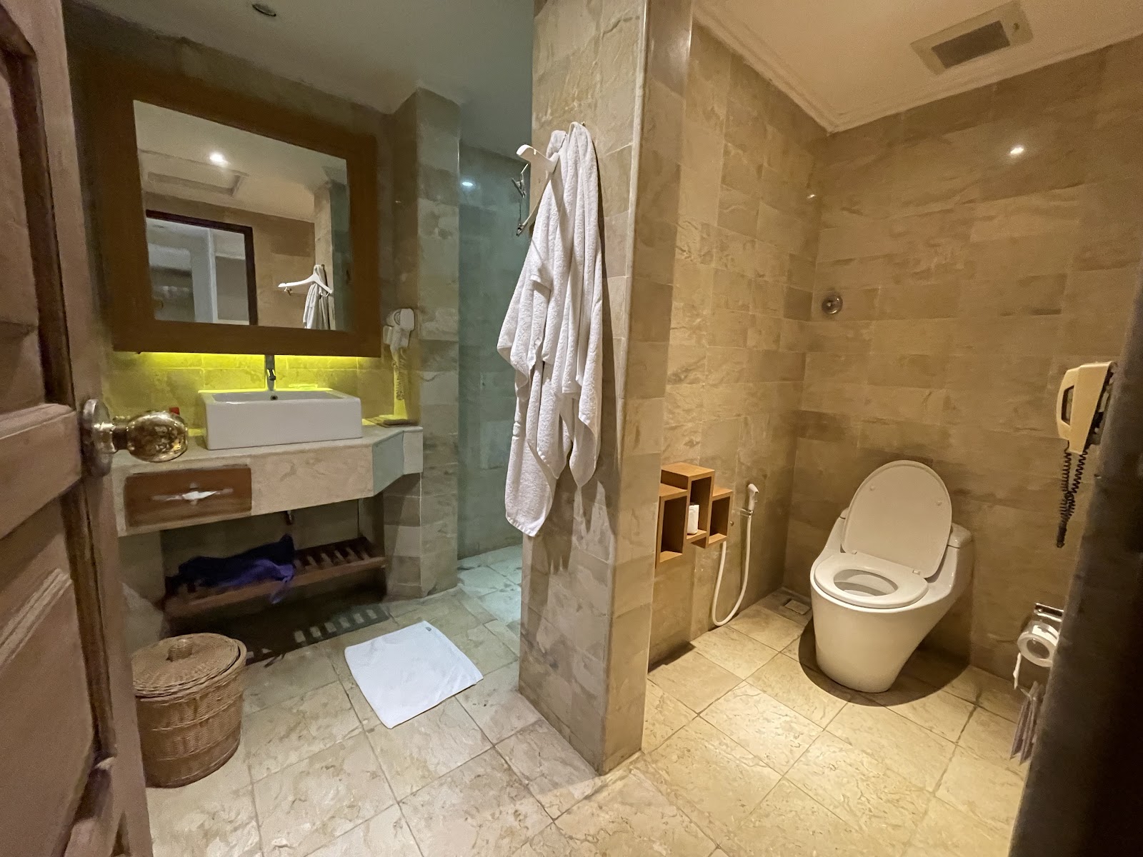 Spacious bathroom with beige tile walls, vessel sink with illuminated mirror, walk-in shower, toilet, and white towels hanging on rack.