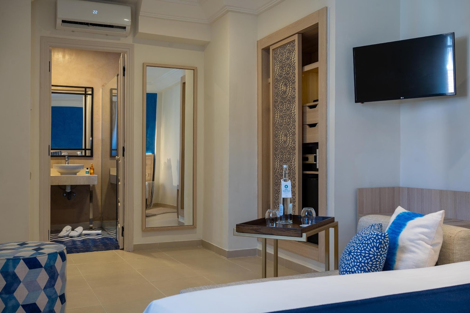 Resort room at Sol Oasis Marrakech with bed, bathroom entrance, wall-mounted TV, and blue accent pillows and decor.
