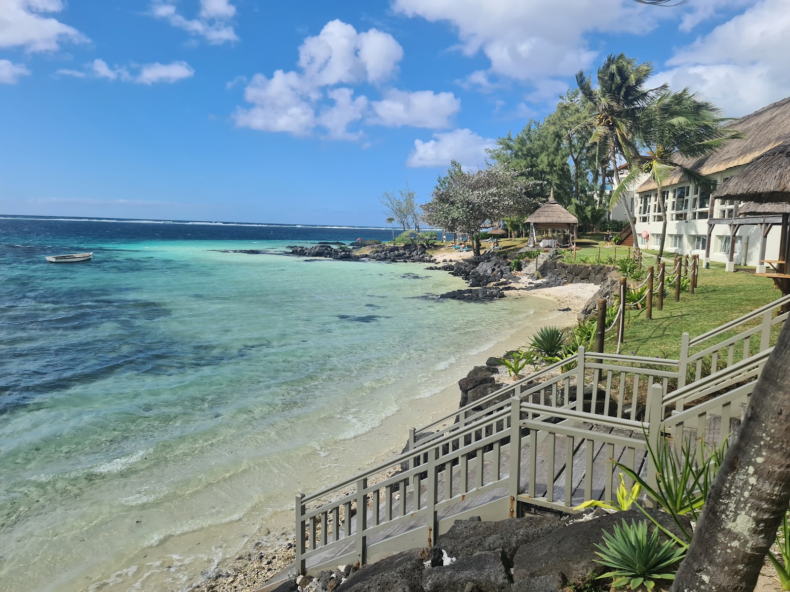 Palm trees frame a sandy beach with thatched umbrellas, lounge chairs, and turquoise lagoon water at Solana Beach Mauritius.