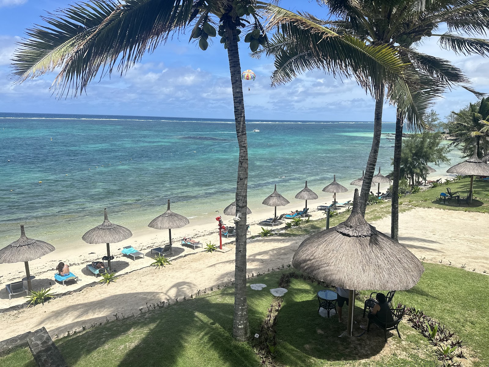Turquoise lagoon waters in front of Solana Beach Mauritius with white buildings and thatched roofs along the sandy beach under clear blue sky.