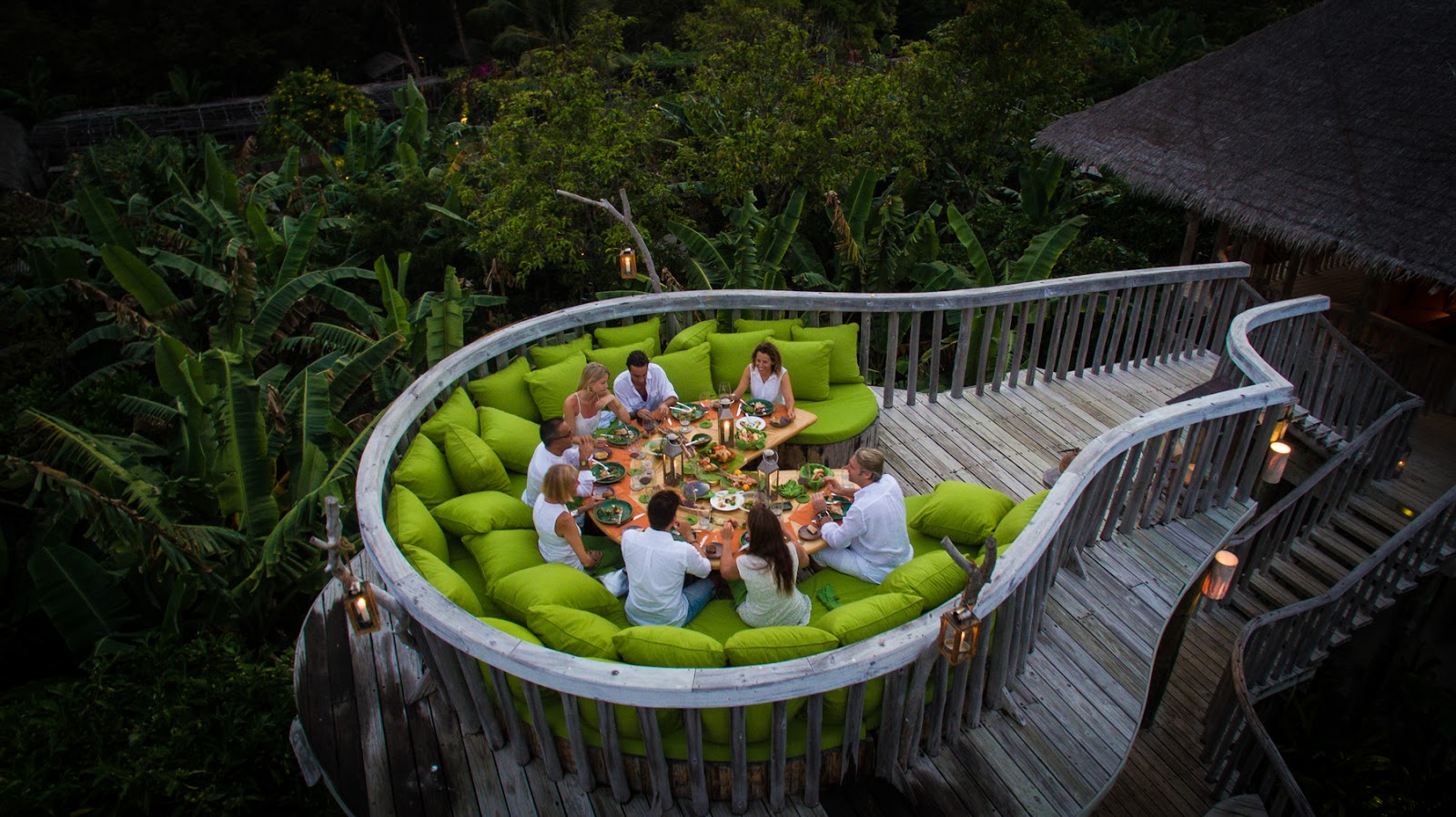 Group dining on a curved wooden platform lined with lime-green cushions, surrounded by tropical vegetation at Soneva Fushi.