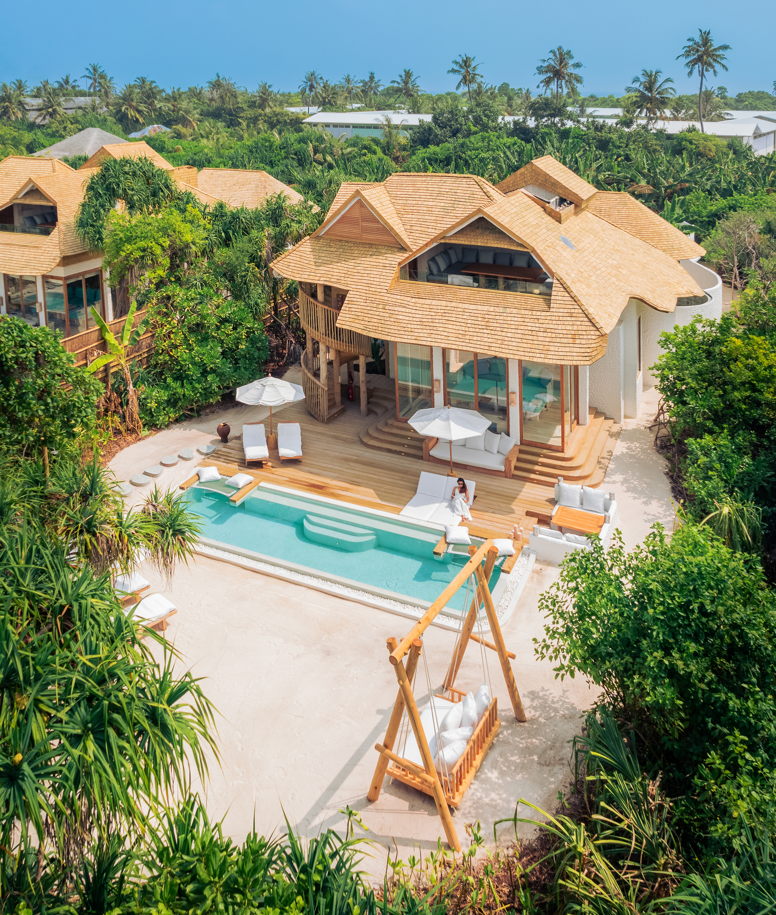 Soneva Jani villa interior with wooden shutters opening to ocean view, beach loungers, and thatched umbrellas at sunset.