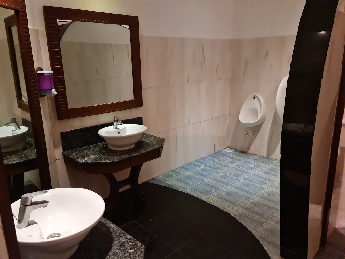 Modern bathroom with two vessel sinks on dark granite counters, framed mirror, urinal, and blue-gray tile flooring at Southern Palms Beach Resort.