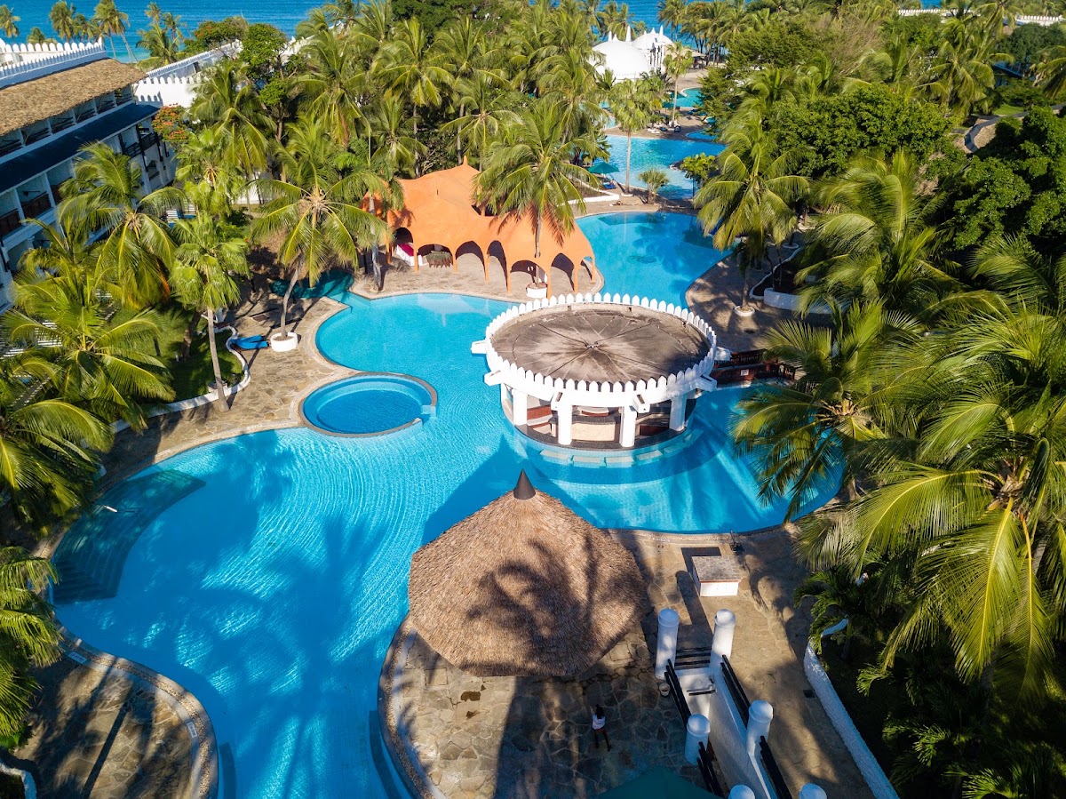 Aerial view of Southern Palms Beach Resort's pool complex with turquoise water, thatched-roof structures, and palm trees surrounding the interconnected pools near the ocean.