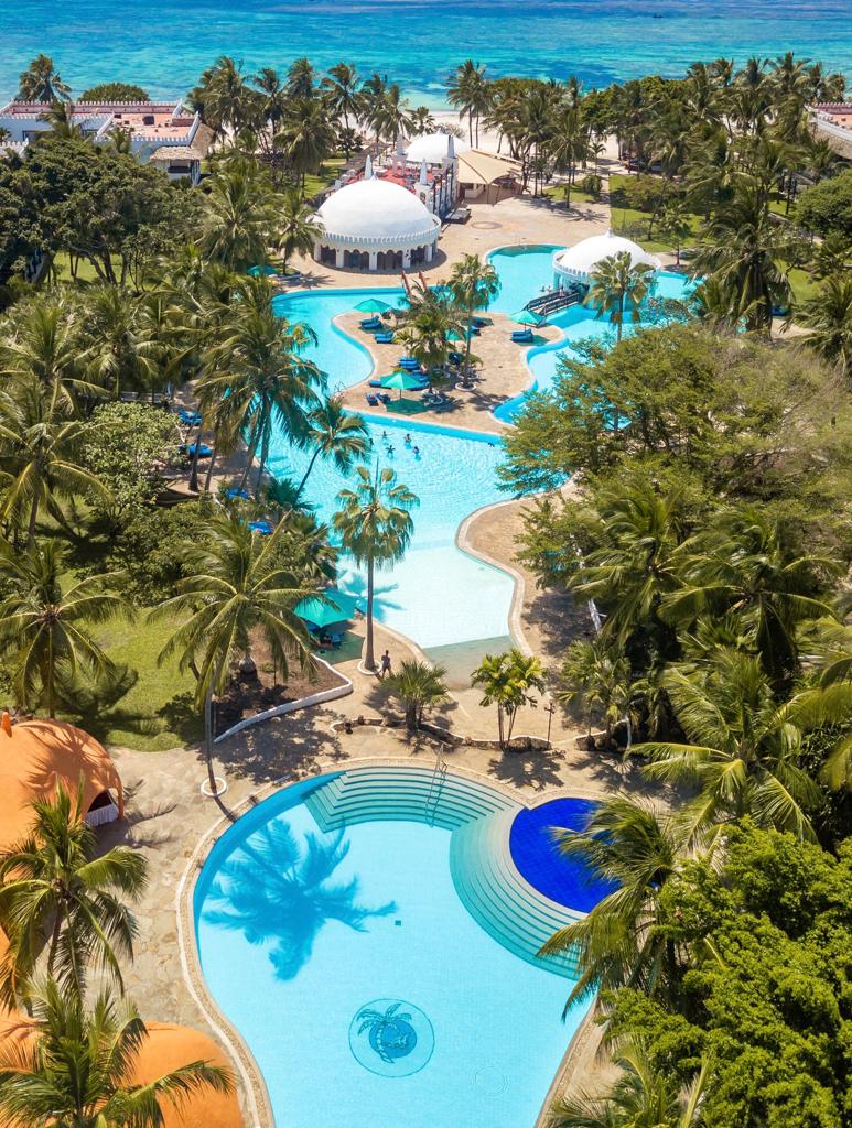 Aerial view of Southern Palms Beach Resort showing multiple pools, a white dome structure, palm trees, and turquoise ocean beyond the beach.
