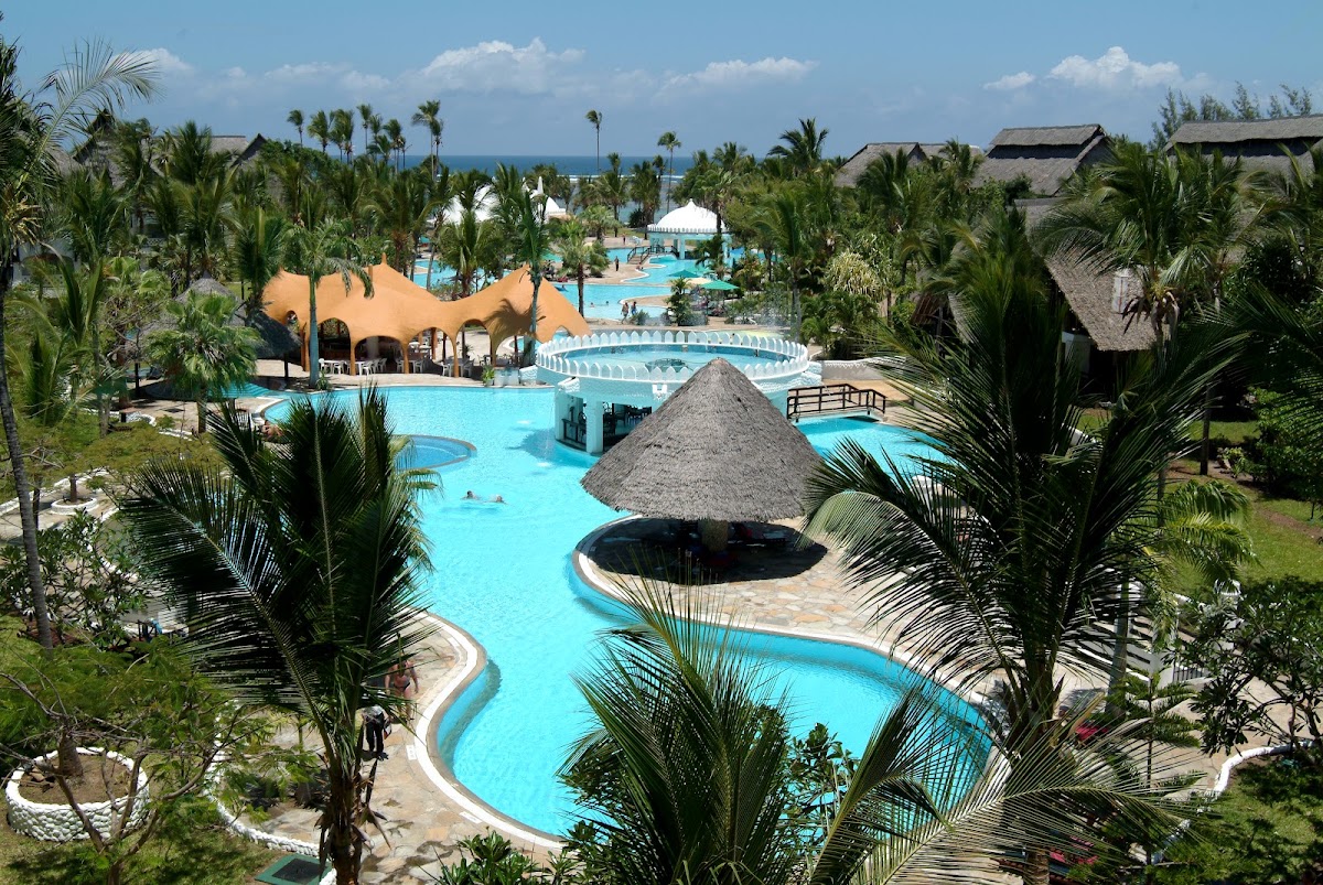 Southern Palms Beach Resort pool complex with turquoise water, thatched-roof structures, and palm trees under blue sky.