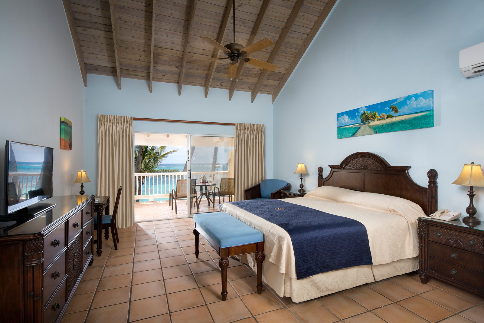 White gazebo with pink floral garland on wooden pier extending into turquoise water at St. James's Club & Villas, with hills beyond.