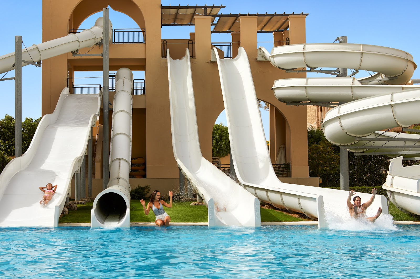 Guests slide down white water slides from a tan multi-story tower into a turquoise pool at Steigenberger Aqua Magic.
