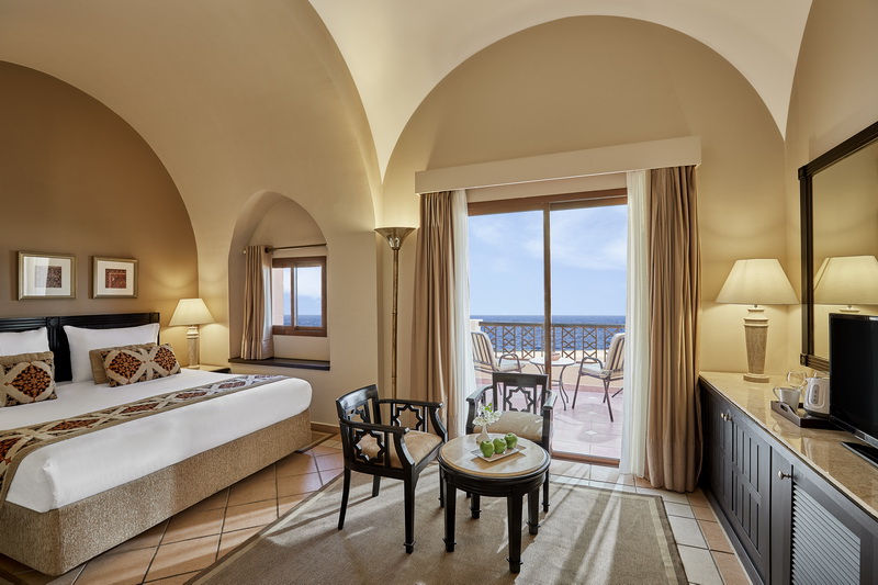 Arched bedroom at Steigenberger Coraya Beach with sea-view balcony, king bed, and sitting area.