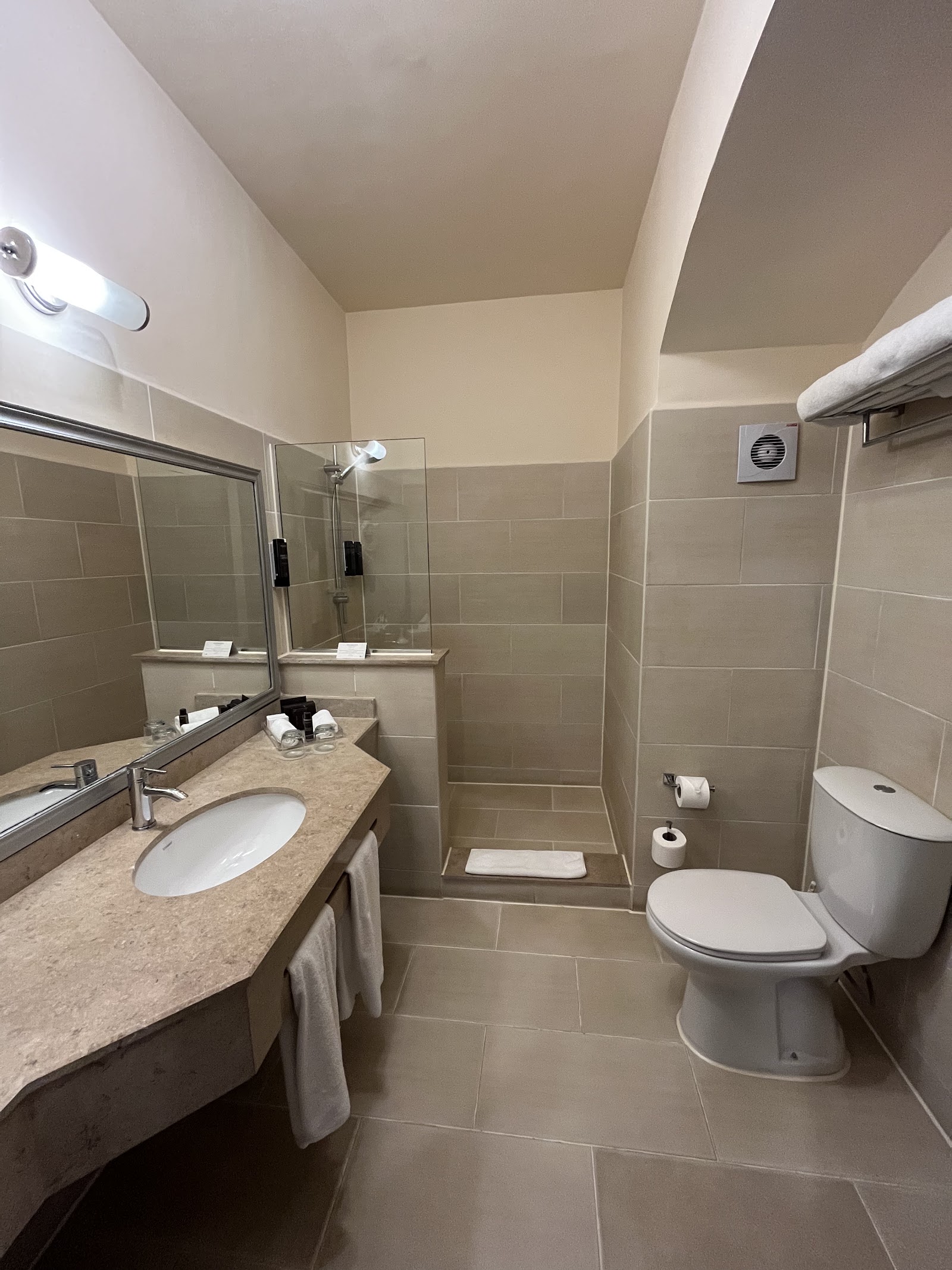 Bathroom with beige tile walls, marble vanity with round sink, glass shower enclosure, and toilet with toilet paper holder.