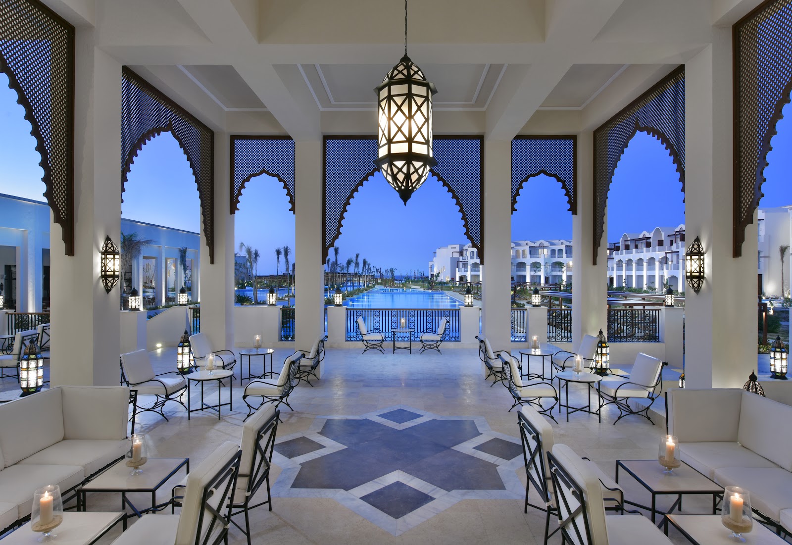 Moroccan-style lounge with arched windows, hanging lantern, and blue pool view at dusk in Steigenberger Resort Alaya Marsa Alam.