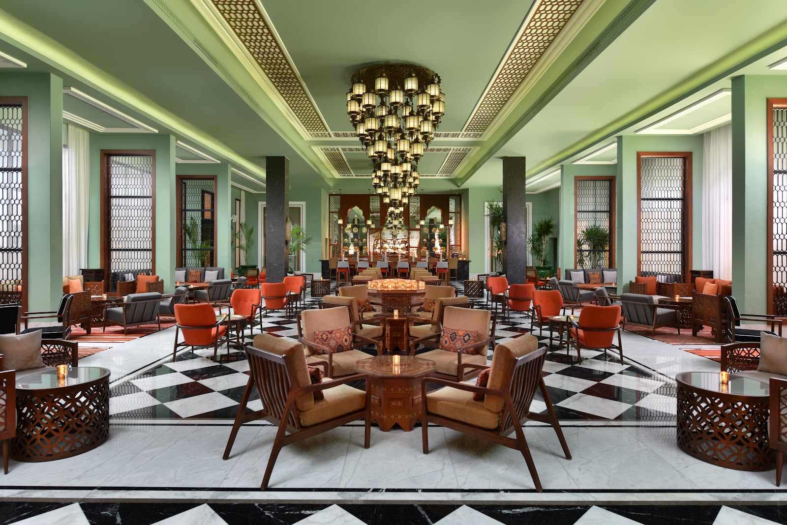 Steigenberger Resort Alaya Marsa Alam's grand lobby features mint-green walls, a cascading brass chandelier, leather seating in orange and tan, and a black-and-white marble floor.