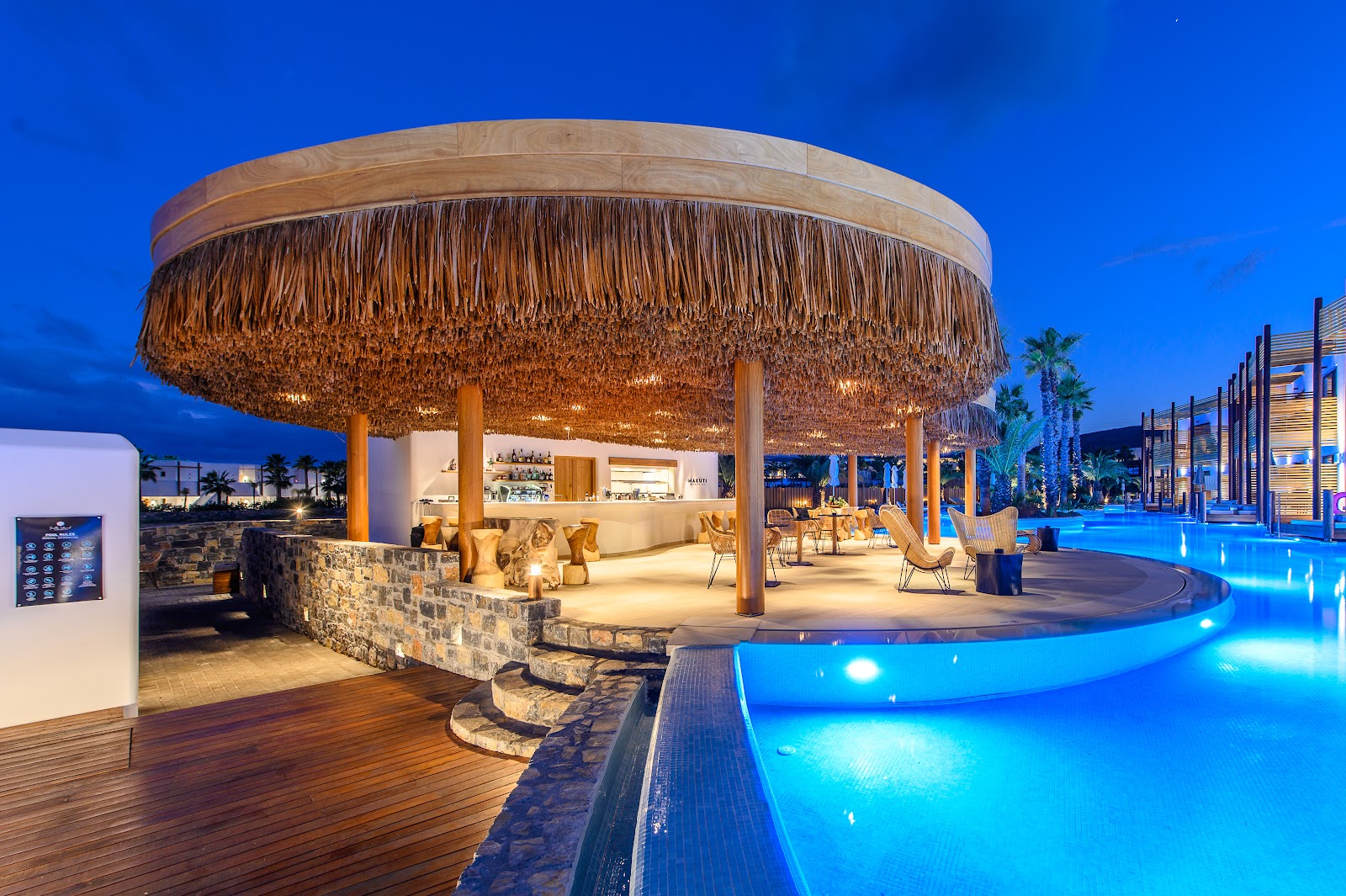 A coral-colored cocktail in a coupe glass sits on a table with blurred palm trees and beach in the background.