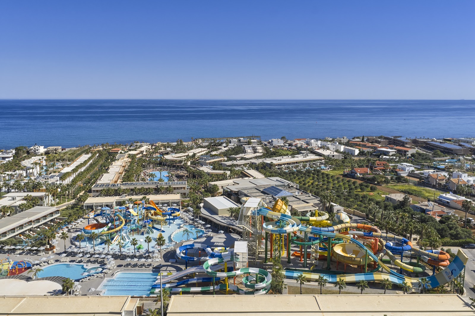 Aerial view of Stella Palace resort showing waterslides, pools, palm-lined grounds, and Mediterranean Sea beyond the beachfront property.