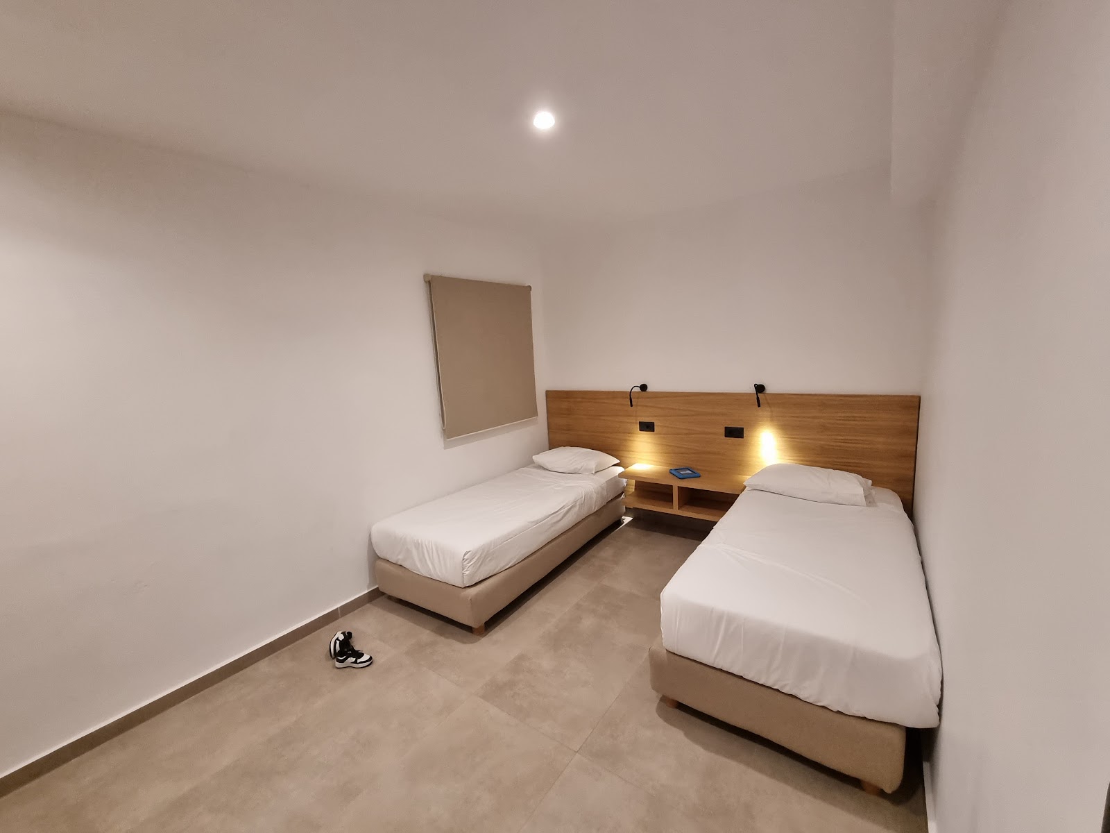Hotel room with two single beds with white linens, wood headboard with reading lights, and beige walls.