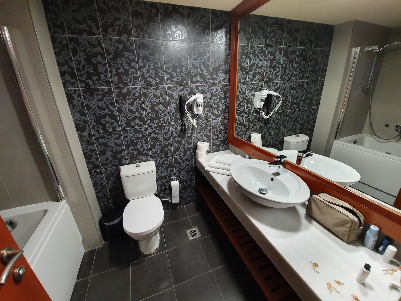 Bathroom with black patterned tile walls, double white sink vanity with wood trim, large mirror, and toilet.