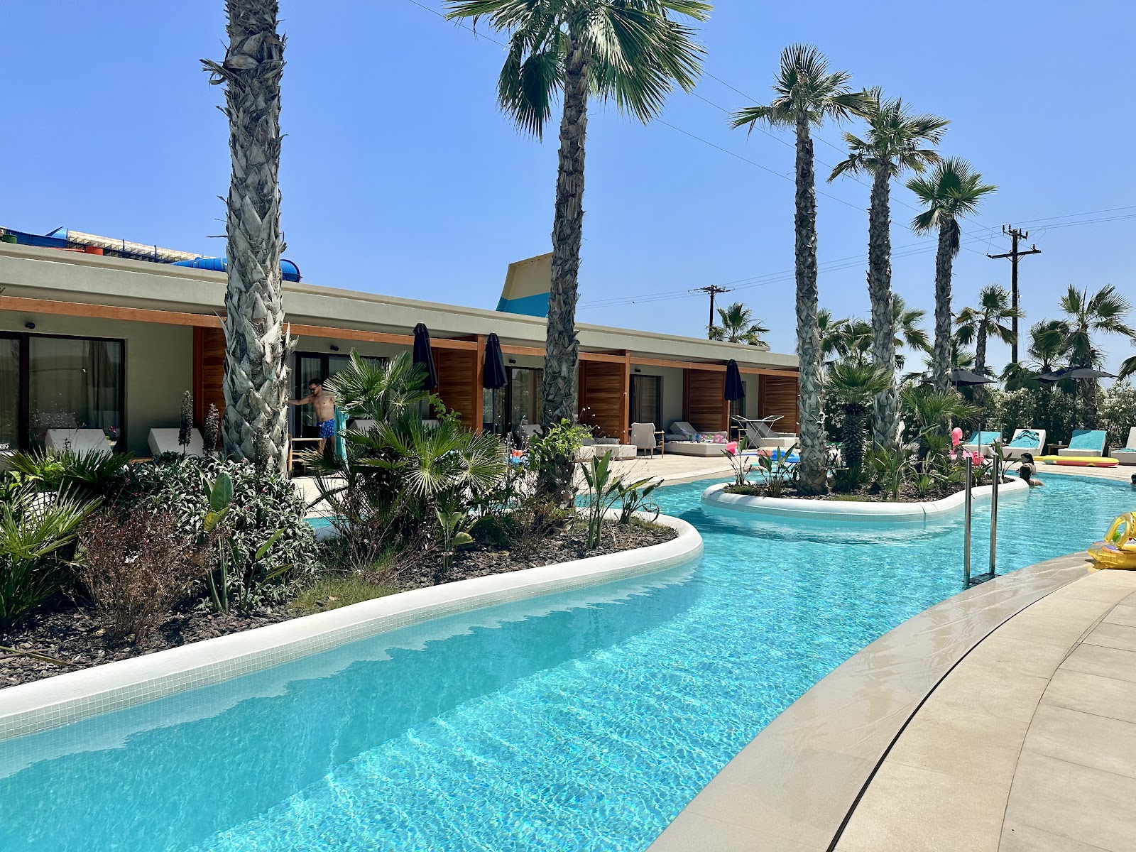 Turquoise pool with palm trees and modern bungalows at Stella Palace resort under clear blue sky.