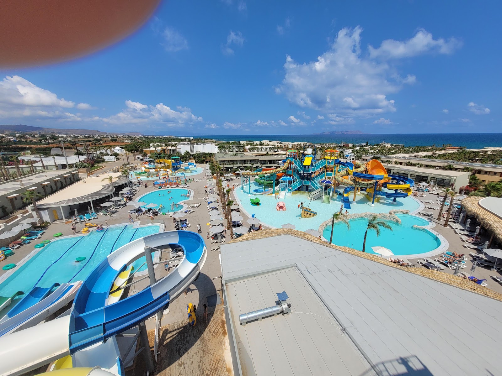 Aerial view of Stella Palace resort's water park with multiple pools, blue and orange slides, and the Mediterranean Sea visible beyond the coastline.