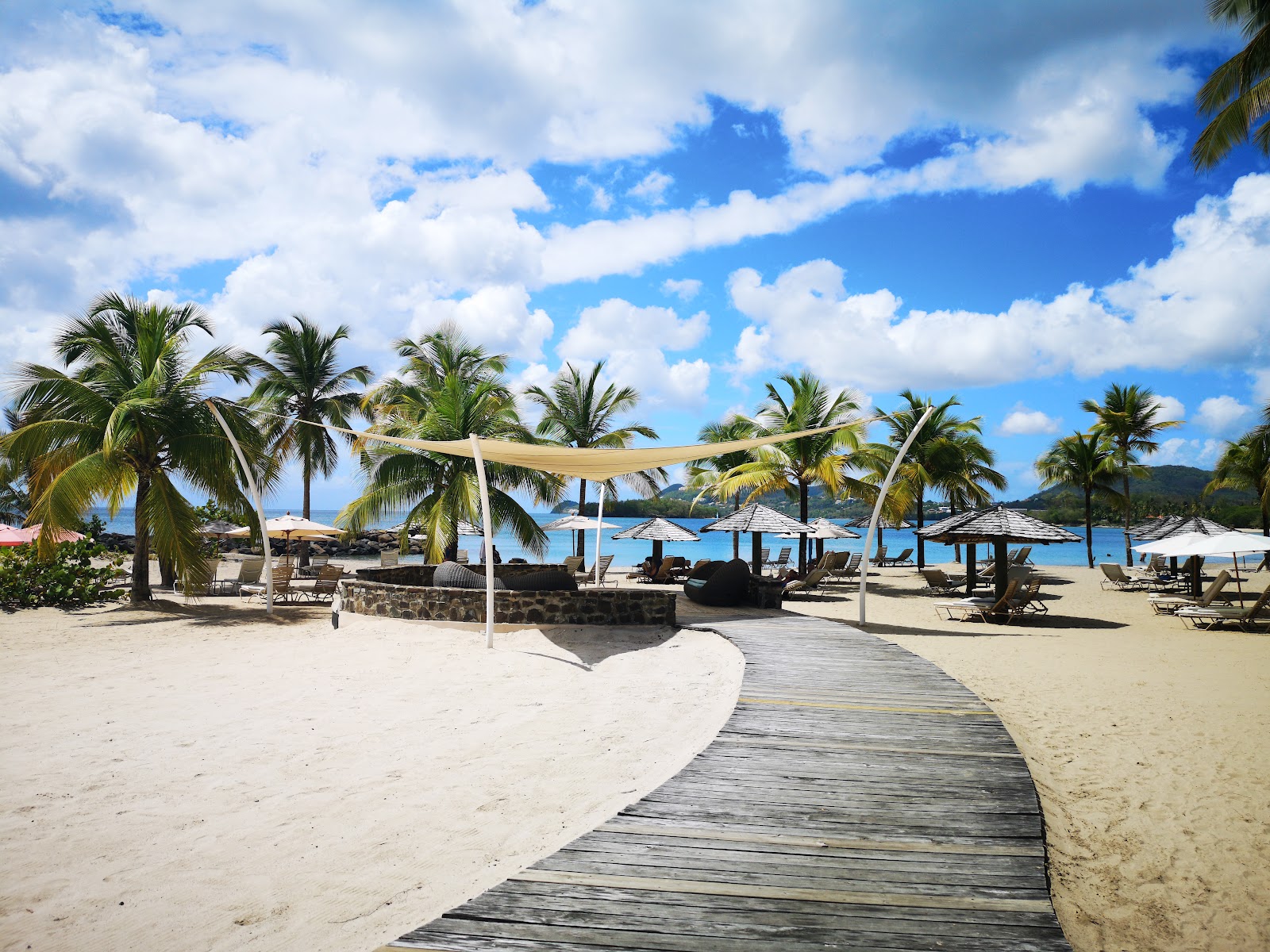Wooden boardwalk leading to a sandy beach lined with palm trees, lounge chairs, and umbrellas overlooking turquoise water at StolenTime by Rendezvous.
