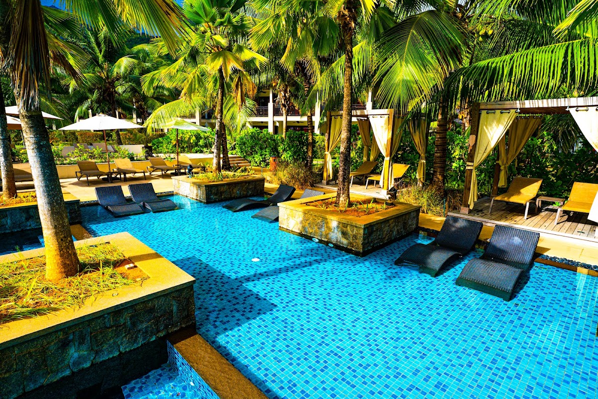 Tiled swimming pool surrounded by palm trees, lounge chairs, and yellow umbrellas at STORY Seychelles.