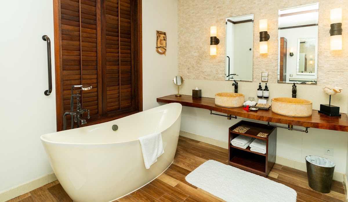 Spacious bathroom with freestanding soaking tub, dual vanity with woven vessel sinks, wooden louvered doors, and stone accent wall.