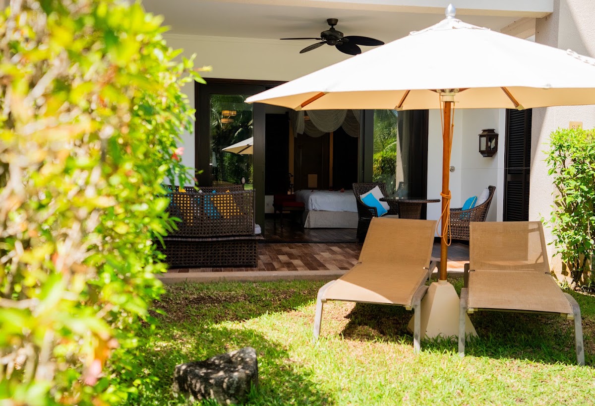 Lounge chairs and white umbrella on grass with tropical greenery framing a beachfront bungalow at Story Seychelles.