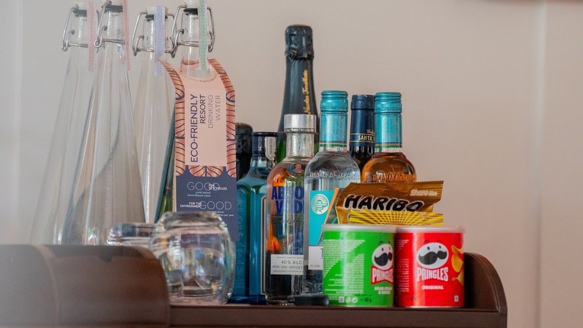 In-room mini bar stocked with bottled beer, spirits, wine, snacks, and candy at Story Seychelles, with reusable water bottles on the shelf above.