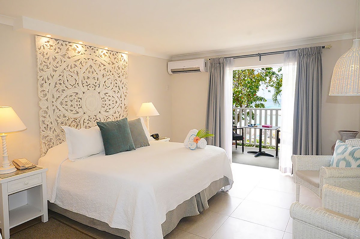 Resort bedroom with white bed, ornate headboard, and open doors to a balcony overlooking tropical vegetation at Sugar Bay Barbados.