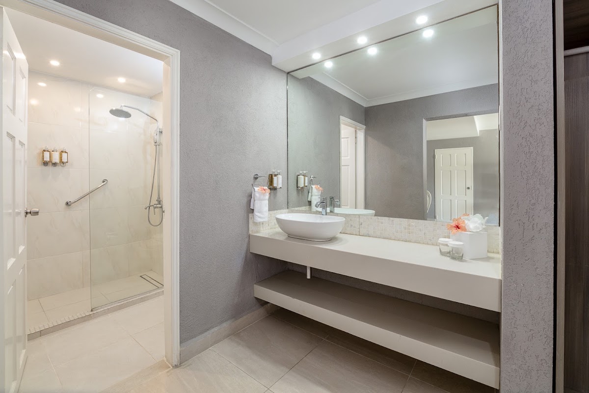 Modern bathroom with gray walls, white floating vanity with round vessel sink, large mirror, and walk-in shower with glass enclosure at Sugar Bay Barbados.