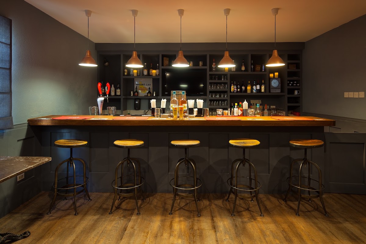 Resort bar with wooden counter, five brass pendant lights, gold barstools, and shelved liquor bottles against dark walls.