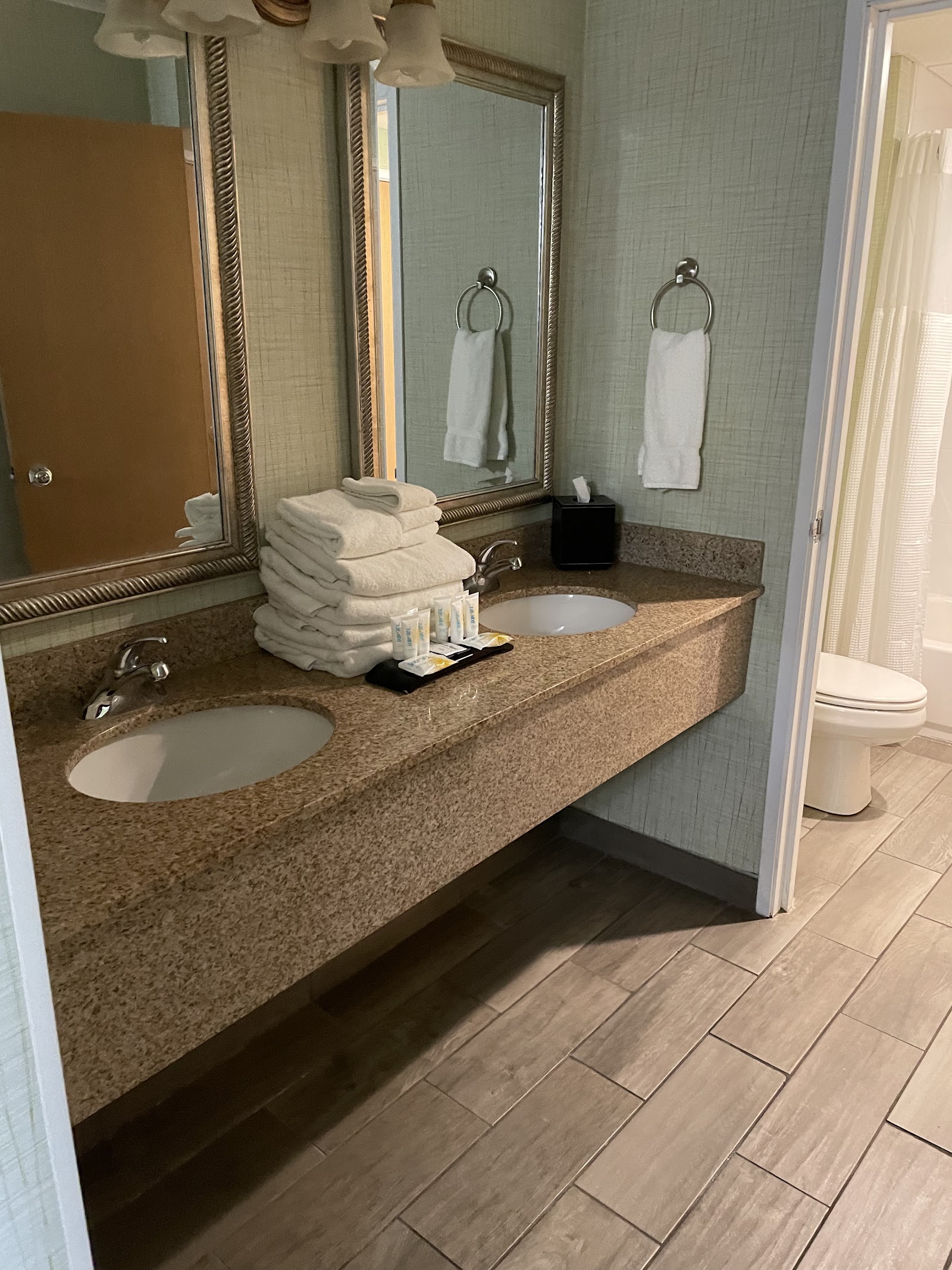 Resort bathroom with dual sinks, granite countertop, stacked white towels, and mirrors with decorative frames.