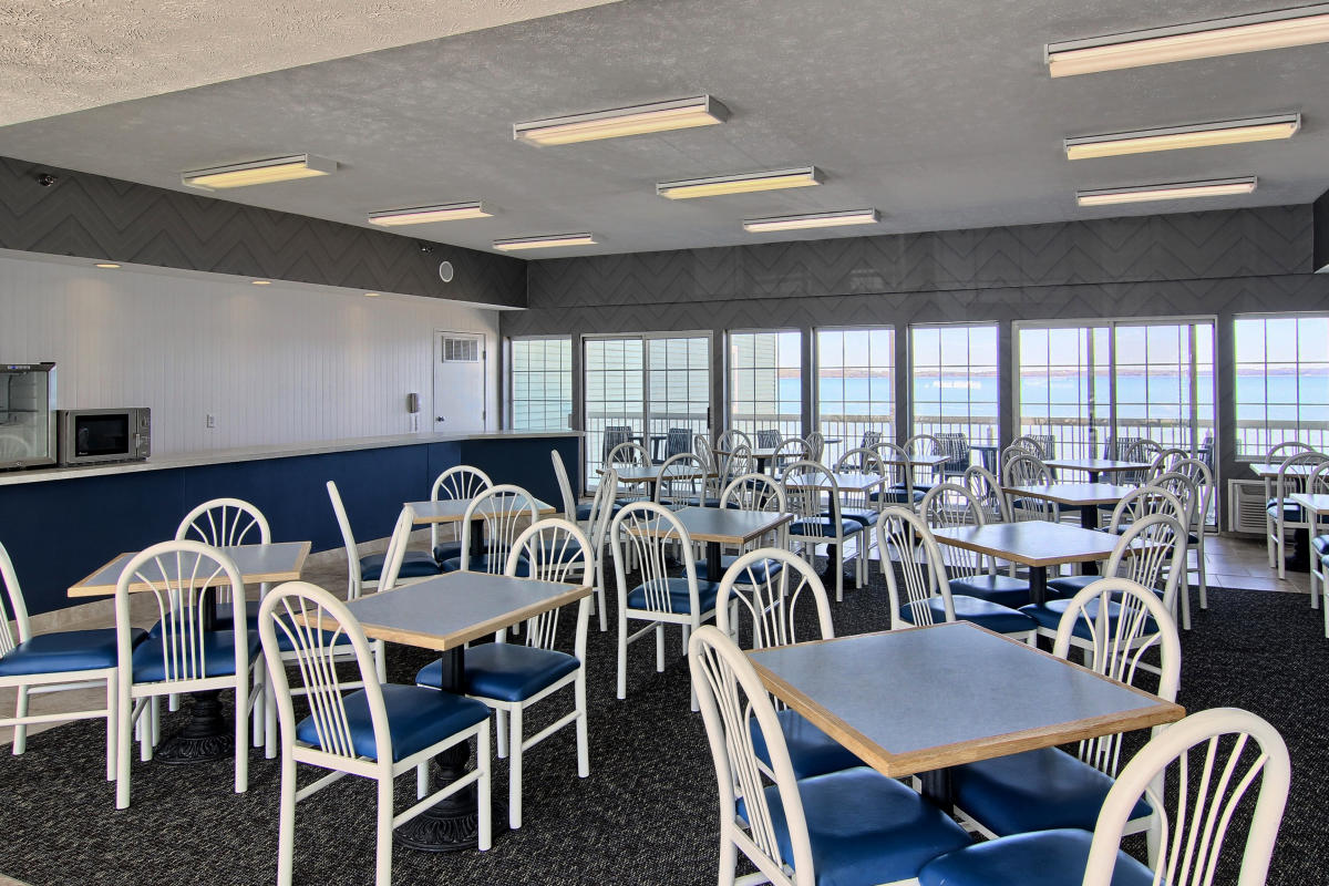 Dining room at Sugar Beach with white fan-back chairs, light wood tables, and blue cushions overlooking the ocean through floor-to-ceiling windows.