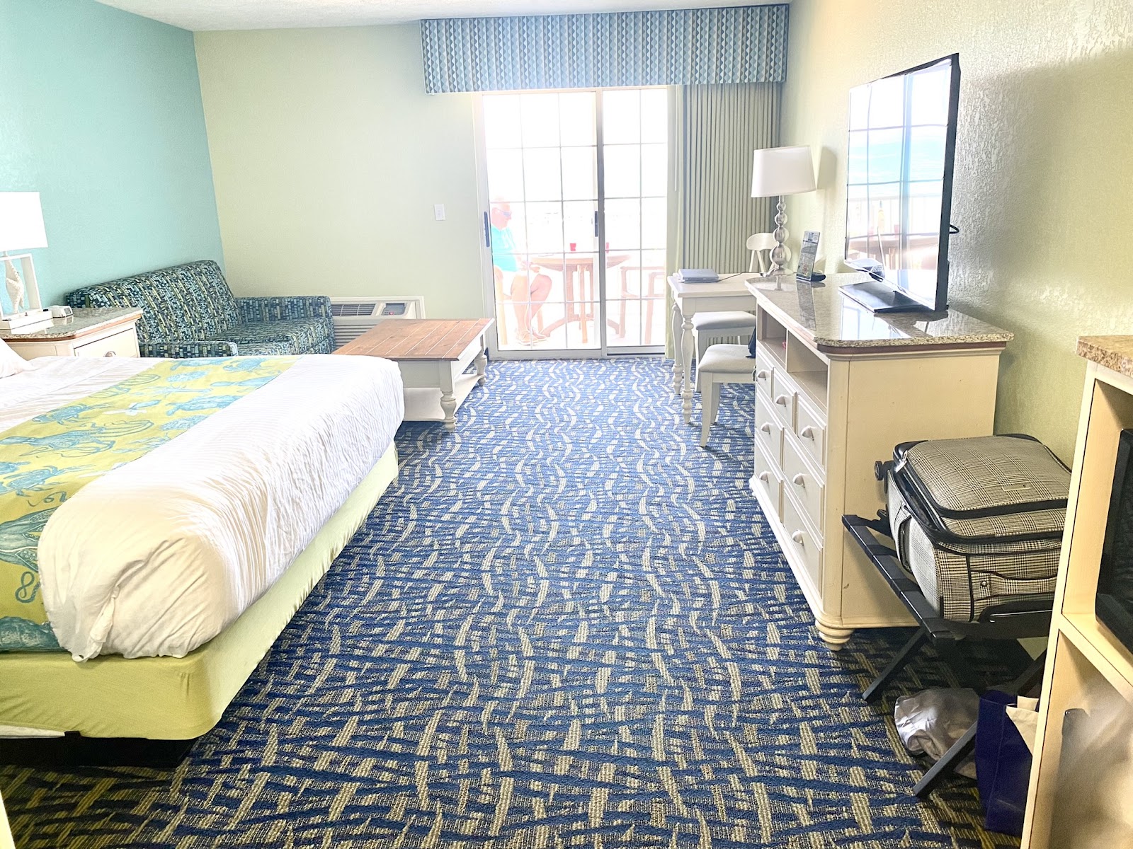 Resort guestroom with queen bed, seating area, desk with monitor, and balcony overlooking the beach at Sugar Beach.
