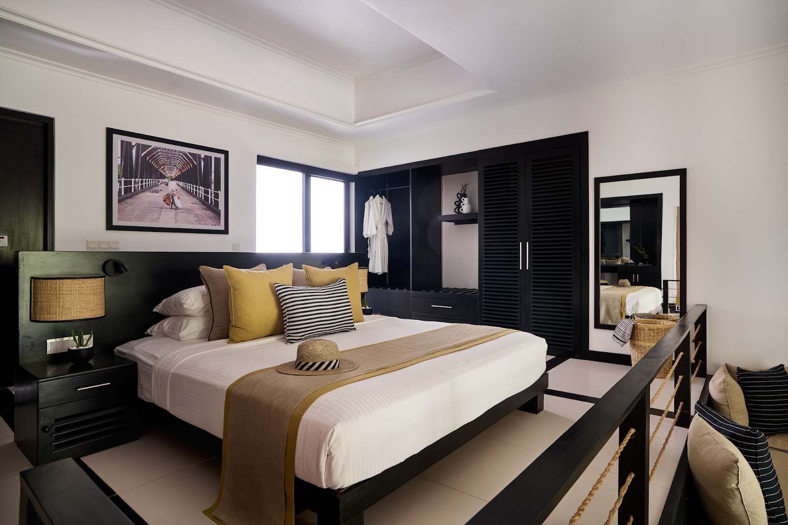 Modern resort bedroom with black bed frame, yellow and striped pillows, white bedding, dark wardrobe, and framed artwork at Sun Siyam Pasikudah.