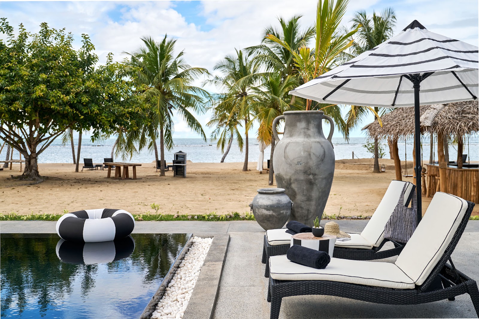 Pool deck with loungers and striped umbrella overlooking palm-lined beach at Sun Siyam Pasikudah, with ocean and thatched structures in distance.