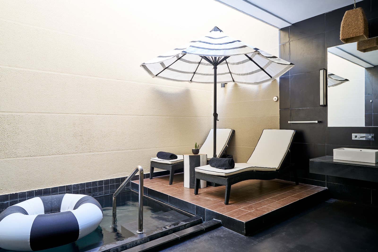Modern bathroom with black walls, dual vanities, glass shower enclosure, woven pendant light, and potted bamboo plant by the entrance door.
