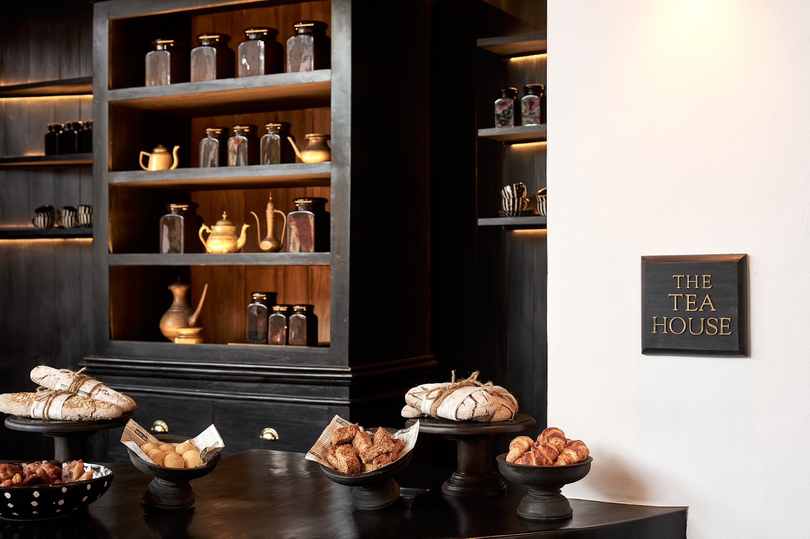 The Tea House display features breads and pastries on black pedestals before illuminated shelving with glass jars and brass teapots.