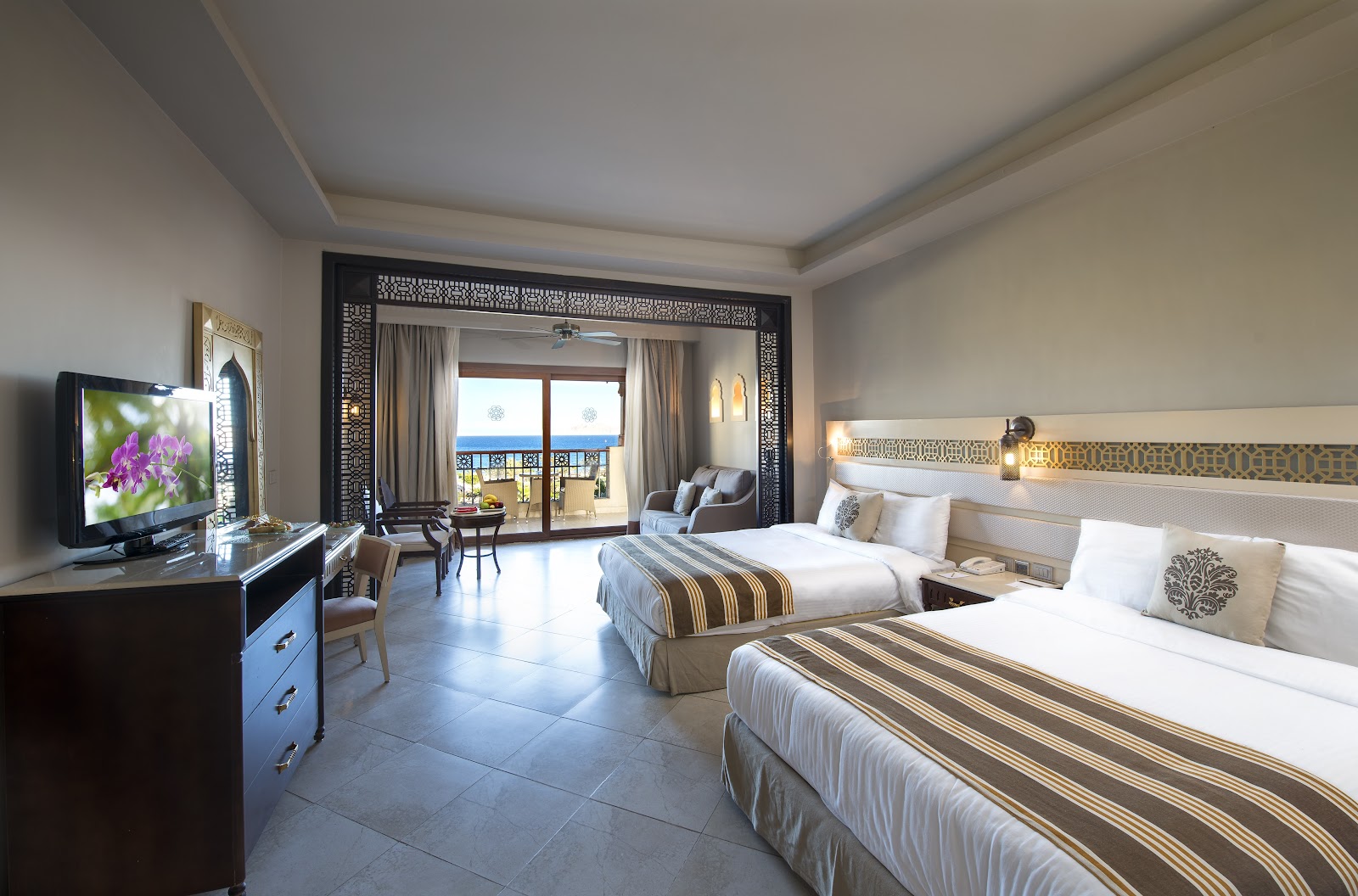 Resort hotel room with two beds, TV, and balcony doors opening to sea view at SUNRISE Arabian Beach Resort.