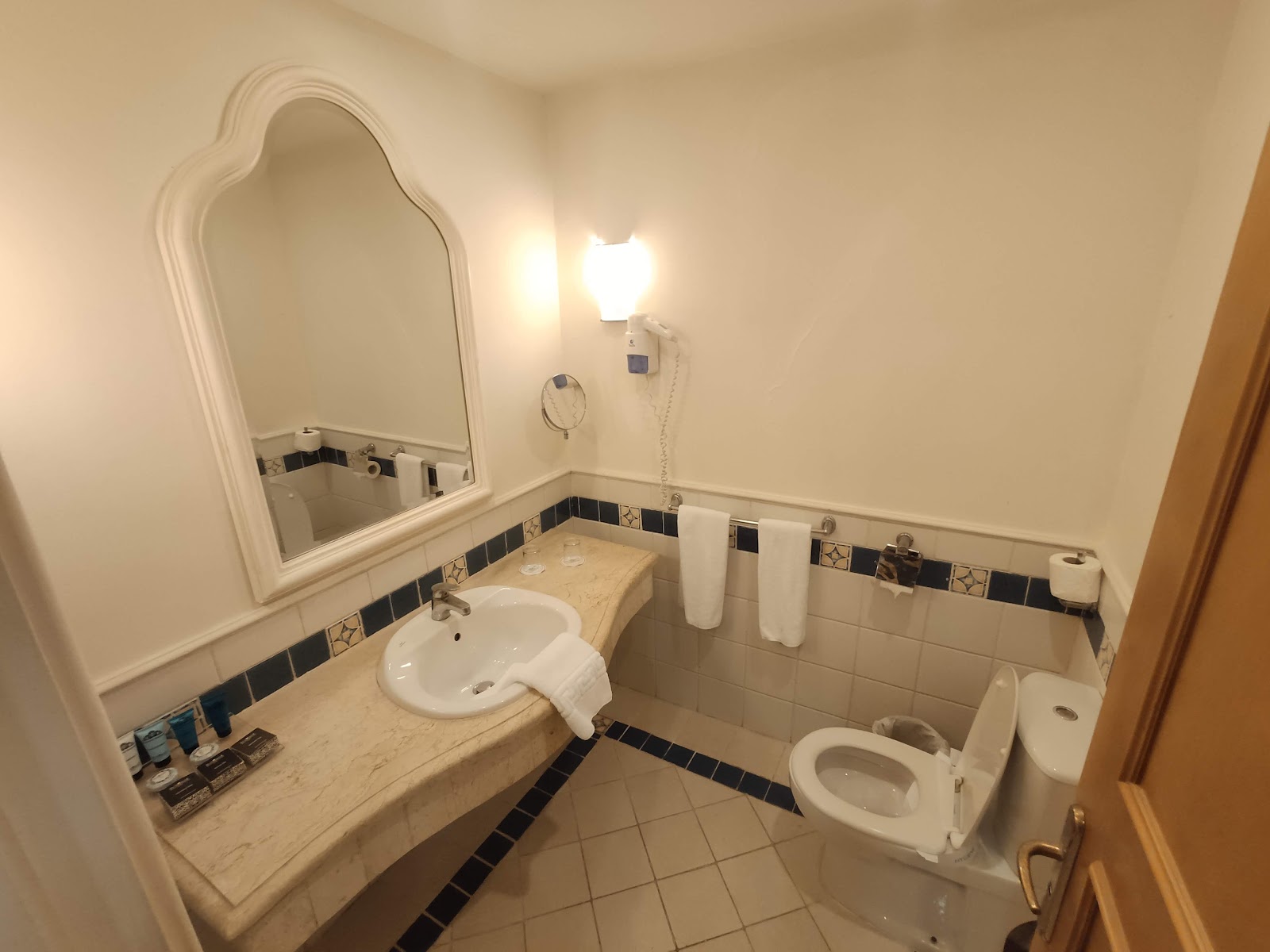 Bathroom with marble countertop, arched mirror, pedestal sink, toilet, and black and white tile accents.