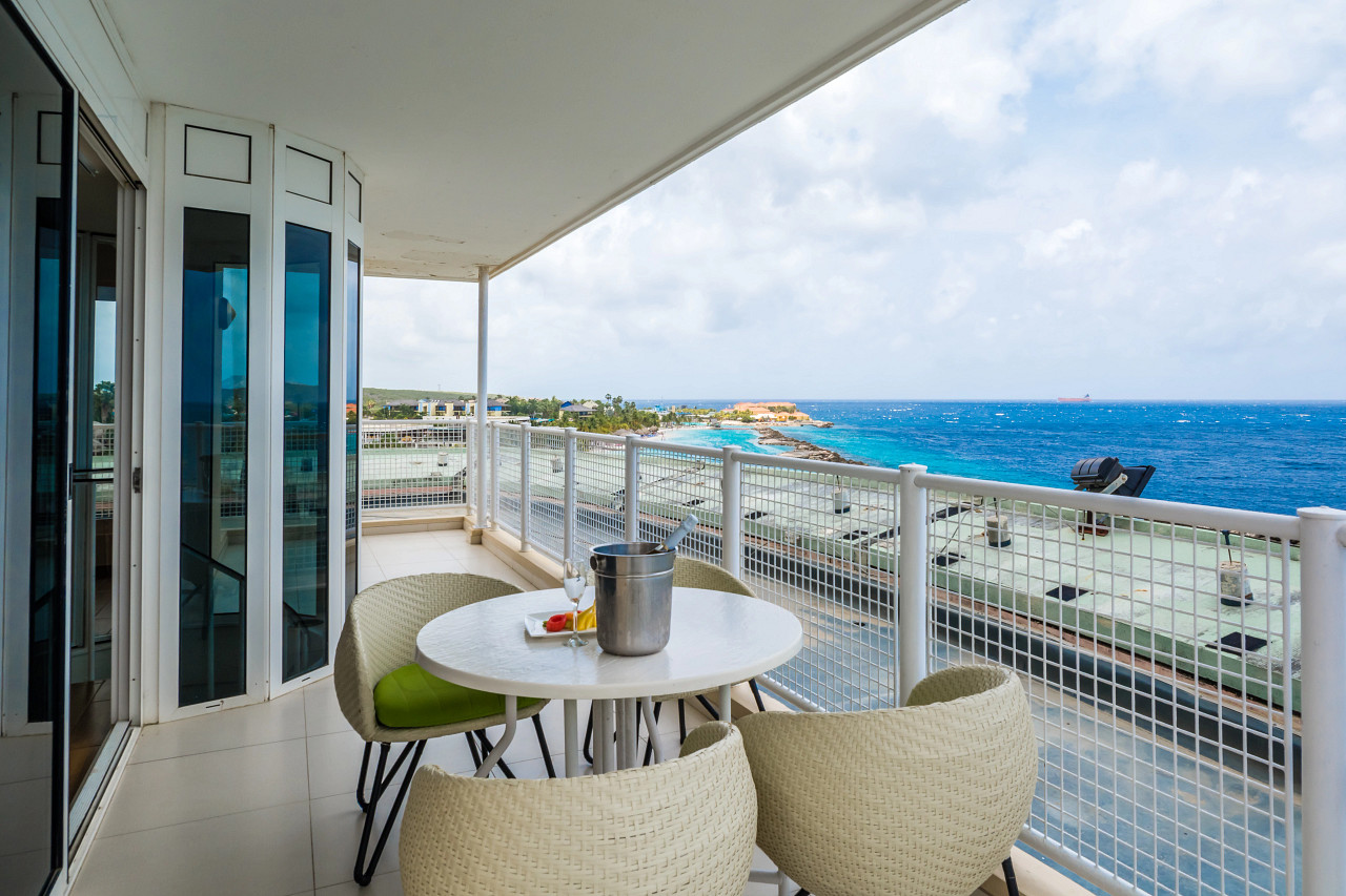 Aerial view of Sunscape Curaçao Resort with multiple pools, beach lounge chairs, thatched palapas, palm trees, and turquoise Caribbean waters.