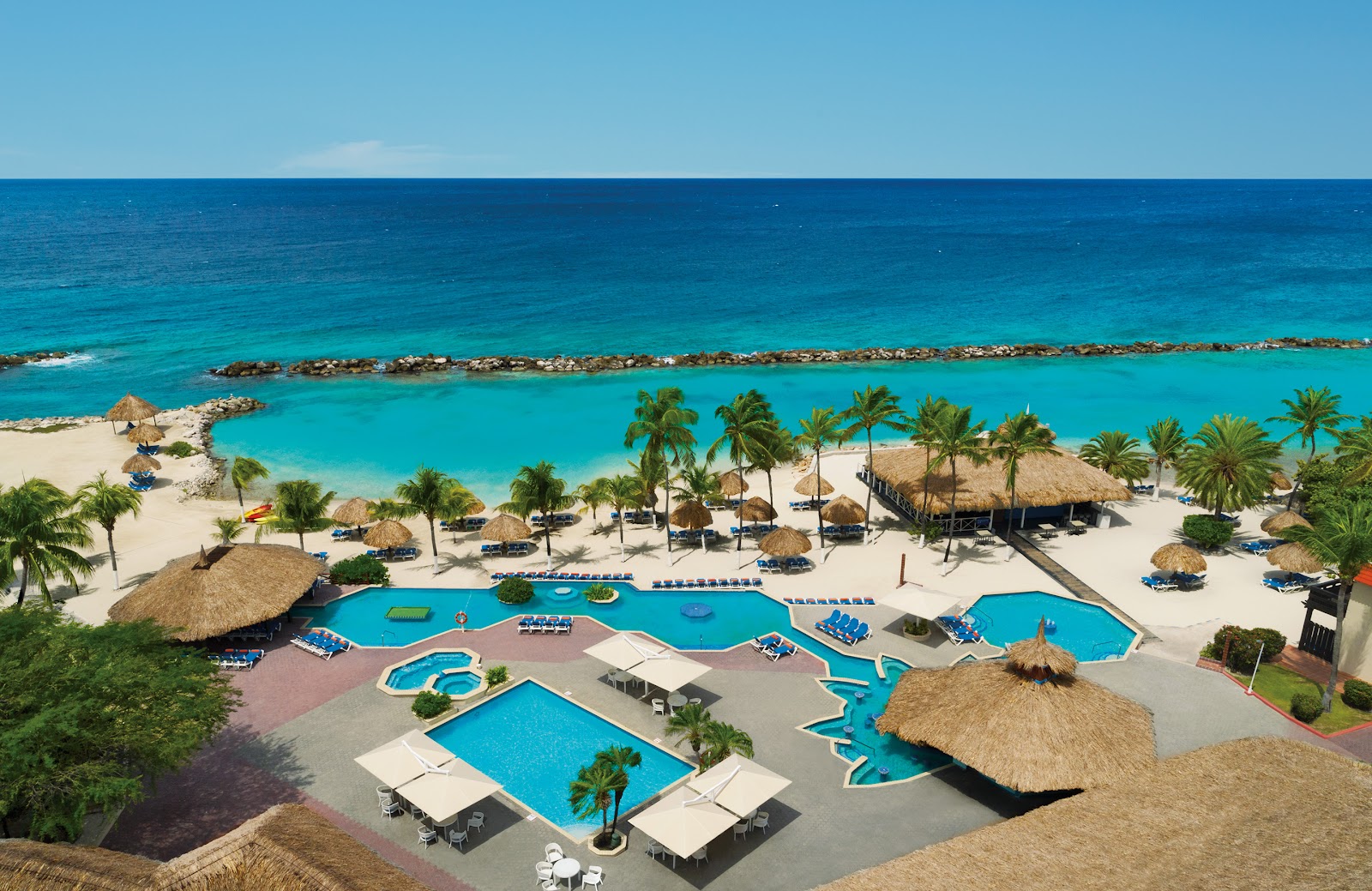 Beach dinner setup at Sunscape Curaçao with illuminated white lounge spheres, colorful seating, and rocky breakwater at twilight.