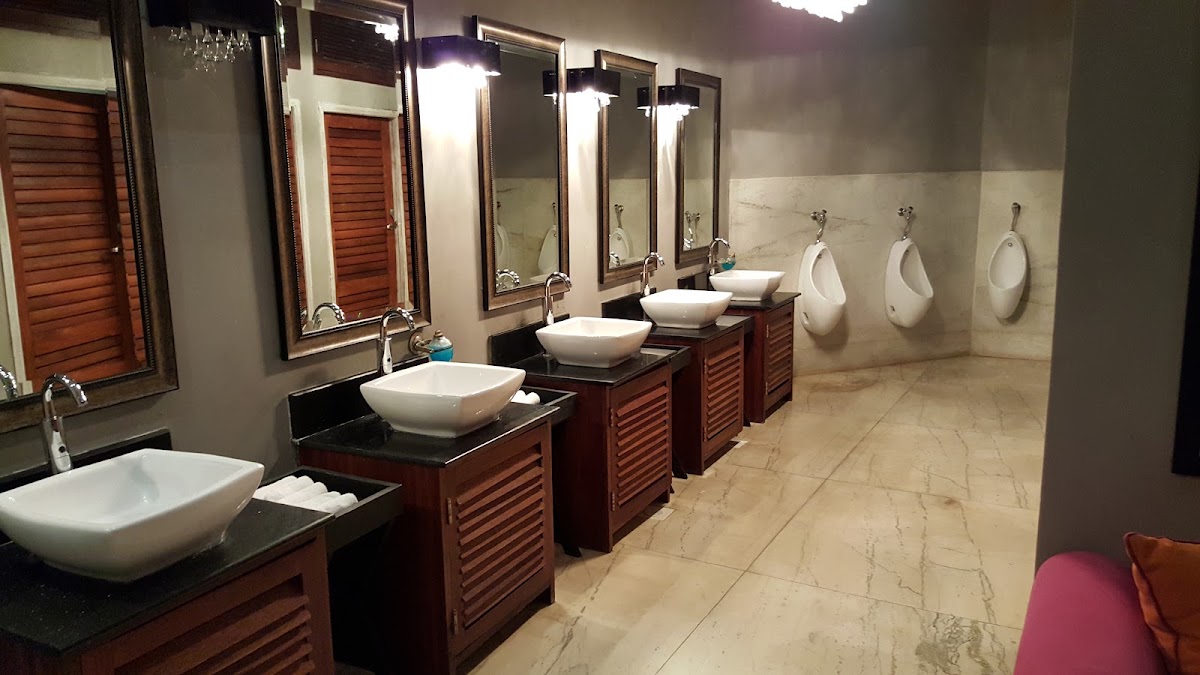 Men's restroom with multiple white vessel sinks, mirrored vanities with wood cabinetry, and urinals along the wall at Swahili Beach Resort.