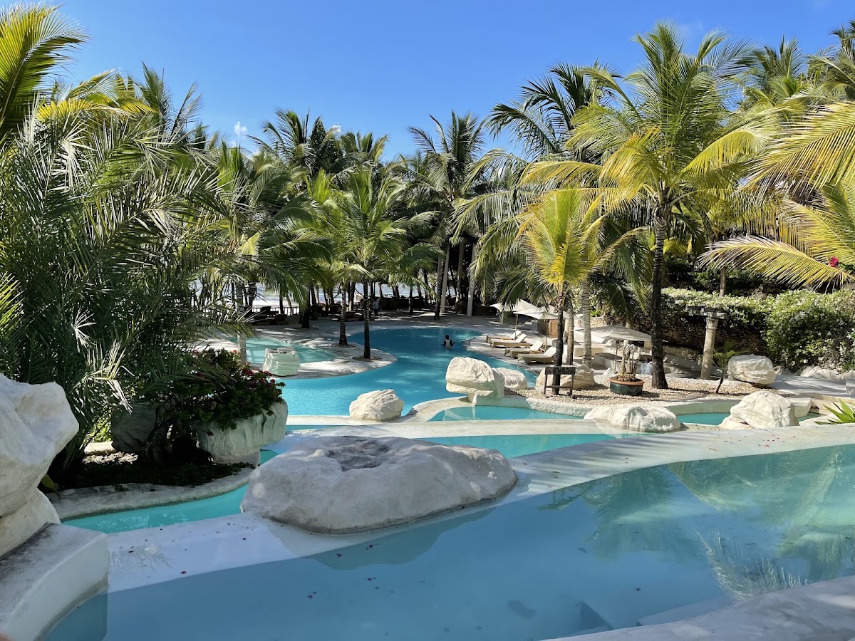 Turquoise lagoon with limestone boulders surrounded by tall palm trees and lounge chairs at Swahili Beach Resort.
