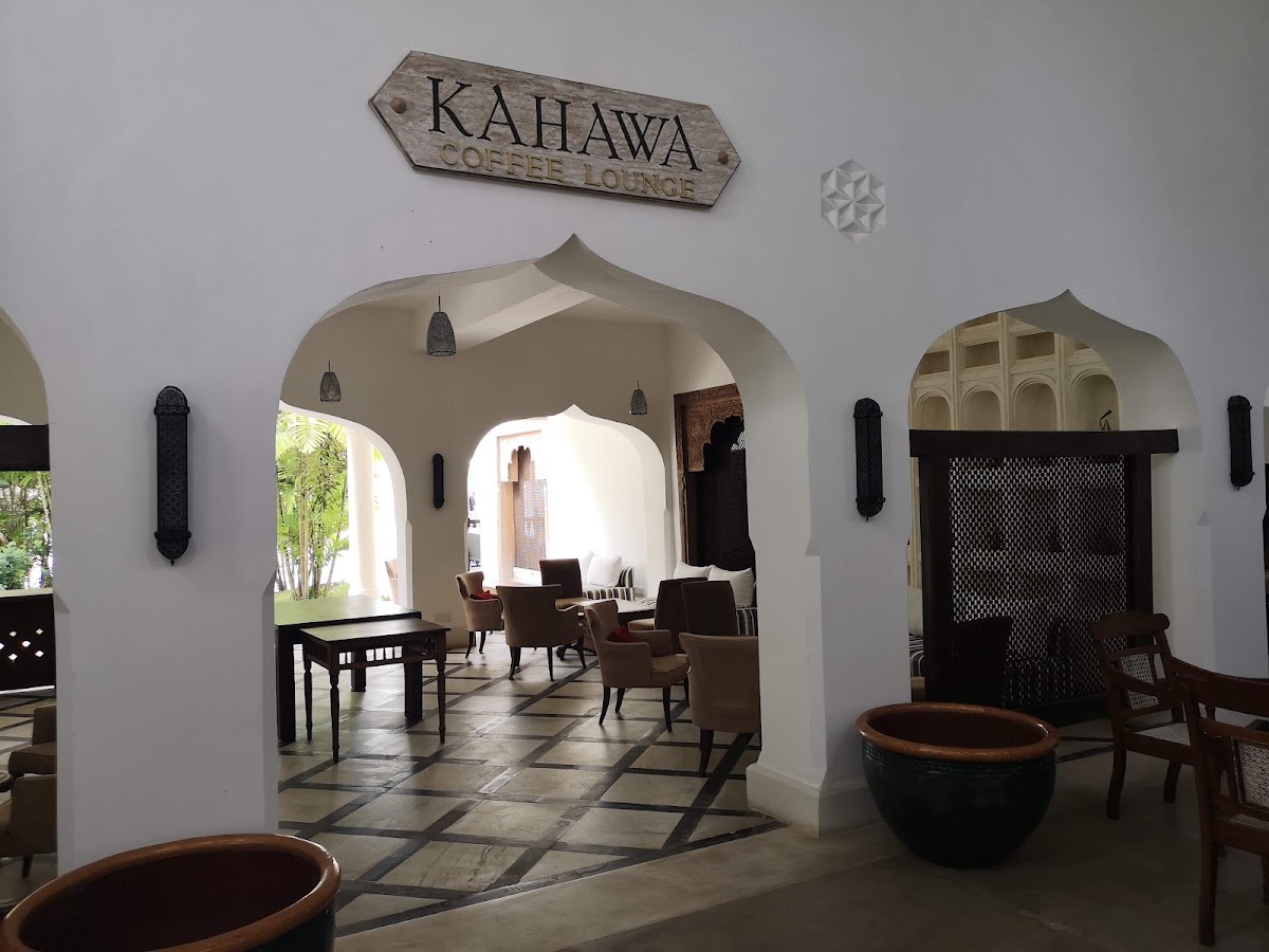Kahawa Coffee Lounge at Swahili Beach Resort features white Moorish archways, dark wooden furniture, and decorative copper vessels on a tiled floor.