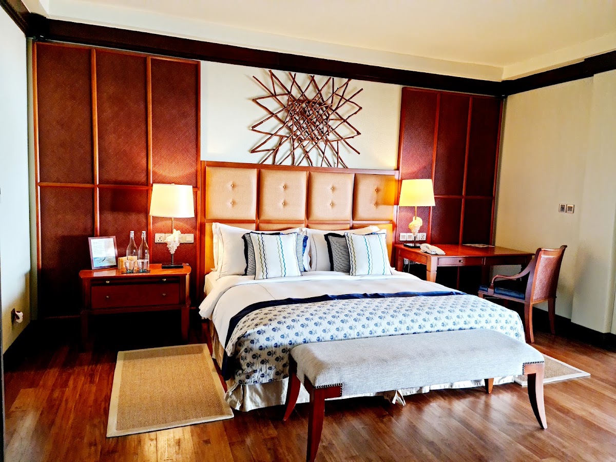Resort bedroom with red-brown wood furnishings, cream upholstered headboard, blue patterned bedding, and geometric wall art above the bed.