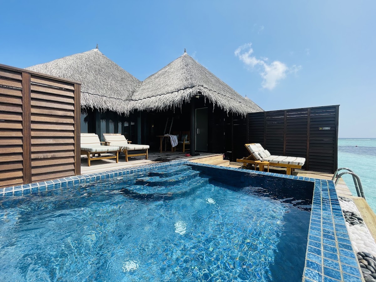 Overwater bungalow with thatched roof, private pool, lounge chairs, and ocean view at Taj Exotica Resort & Spa Maldives.