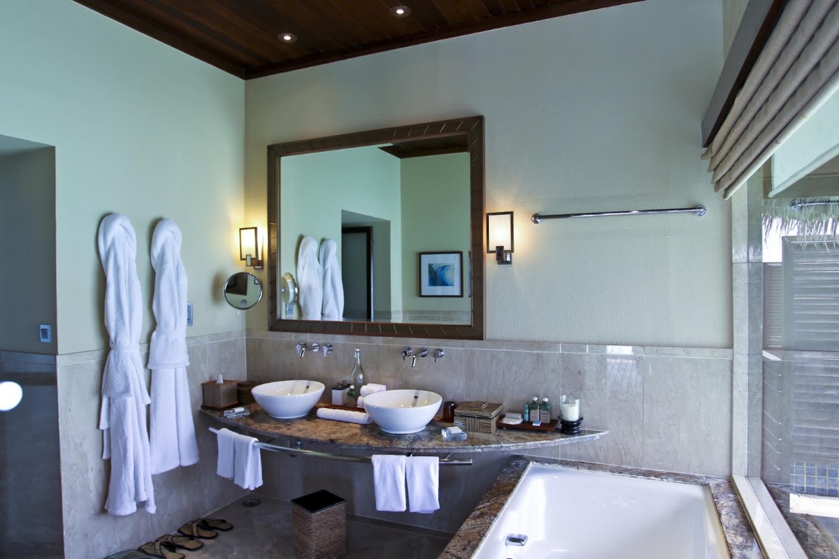 Bathroom with double vessel sinks, large mirror, soaking tub, and white towels at Taj Exotica Resort & Spa Maldives.